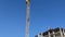 Cranes Near An Apartment Building. Construction Cranes on the Background of the Blue Sky and the Bright Sun.