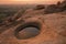 A crater with water inside formed on the top of the Hanuman mountain in Hampi, India. The photo is taken at a red sunset dusk