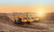 Crawler excavator in the rays of the setting sun at sunset digs earth and sand at a construction site for the construction of the