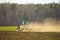 Crawler Tractor plowing ploughing field with Harrow in Spring on Farm with Dust Clouds