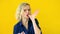 Crazy cheerful blonde girl licks fingers after tasty eating isolated on yellow studio background. Sweets. 4k footage