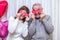 Crazy couple seniors celebrate Valentine's Day. Man and woman cover eyes with red valentine cards and smile. Romantic