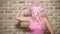 Crazy girl with pink curly hair demonstrates her biceps against a brick wall. copy space. concept of humor, adventures