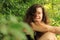 Crazy girl woman with long unkempt brown hair and mad look of her face in the middle of green vegetation in forest or wood