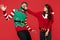 Crazy image of couple dressed in Christmas funny sweaters over red background. Punch in the jaw.