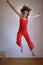 Crazy positive young brunette woman in red overalls jumping up from wooden stool at home