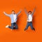 Crazy teenage guys jumping and fooling over orange background