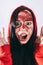 Crazy woman posing in a red hoodie with a painted face. Bizarre portrait with painted face