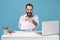 Crazy young bearded man in light shirt work at white desk with pc laptop isolated on pastel blue background. Achievement