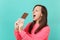 Crazy young girl in knitted pink sweater keeping eyes closed hold in hand biting chocolate bar isolated on blue