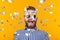 Crazy young positive hipster guy with a beard laughs happily among flying kofetti on a yellow background. The concept of