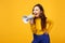 Crazy young woman in sweater, blue trousers looking aside and scream in megaphone isolated on yellow orange wall