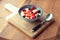 Cream and berries dessert in deep clay bowl on wooden board, ton