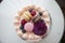 Cream cake seen from above, with macarons, blueberries, raspberries, purple flower and pearls