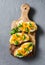 Cream cheese, roasted yellow bell pepper, basil bruschetta on cutting board on grey background
