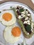 Creamy avocado on sourdough bread topped with pomegranate seeds and crumbled feta cheese served with two medium fried eggs