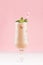 Creamy cold fresh beverage in elegant transparent glass with ice cubes, green mint and striped straw  in modern light pink color.