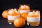 Creamy panna cotta with orange jelly in beautiful glasses, fresh ripe mandarin on wooden section on black background. Delicious It
