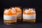 Creamy panna cotta with orange jelly in beautiful glasses, fresh ripe mandarin on wooden section on black background. Delicious It