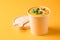 Creamy pumpkin fall soup in craft paper food container with bamboo spoon against orange background with copy space