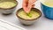 Creamy pureed celery soup served with fresh basil leaves close up in a bowl on kitchen table, woman hands