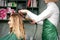 Creating curls with curling irons. Hairdresser makes a hairstyle for a young woman with long red hair in a beauty salon.