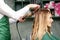 Creating curls with curling irons. Hairdresser makes a hairstyle for a young woman with long red hair in a beauty salon.