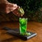 Creating of refreshing drink. Male hand puts teaspoon of kiwi fruit in glass with green mint beverage. Healthy natural