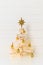 Creative alternative Christmas tree made of wooden sticks, decorated golden balls and garland on background white wall.