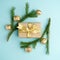 Creative Chistmas layout made of winter greenery, kraft gift box with golden ribbon and golden decoration on blue background.