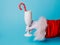 Creative Christmas composition with Santa Claus hand holding champagne glass and candy cane on blue background. Minimal Xmas or Ne