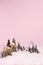 Creative Christmas scene made with with ginger houses, Santa Claus, trees, snow and reindeers on pink pastel color background