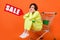 Creative collage of unsatisfied girl sitting empty shelf supermarket shopping card isolated on orange color background