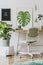 Creative composition of home workspace interior design with mock up poster frame, table, plants in hipster designed pots.