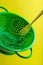 Creative concept with levitated green colander, plug headphones and fork on yellow background