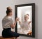 Creative conceptual collage. Excited young girl looking in mirror and seeing reflection of little girl, her child self