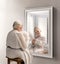 Creative conceptual collage. Senior lady, woman looking in mirror with reflection of little girl, child. Younger self