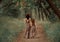 Creative family photo of brunette mother and blond daughter, fauns hold hands and go deep into the forest along an