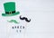 Creative festive St Patricks background with photobooth props moustaches and glasses with shamrock on white wooden table.