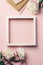 Creative flat lay with flowers, notebook, glasses, mobile phone and white wooden frame on pink background