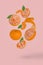 Creative food concept with fresh ripe whole and sliced mandarine flying in air isolated on a light pink background