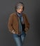 Creative gray-haired woman in casual on gray, portrait. Lady in jacket, colorfull scarf and jeans smiles looking down