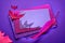 Creative Halloween background in glowing neon pink and purple with stack of glittering paper, quill and paper bats. Copy-space on