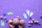 Creative Halloween flat lay on purple paper background with paper ghosts, spiders, stars and chocolate candy eyes. Hands holding