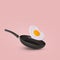 Creative idea with a frying pan and a flying fried egg in heart shape on a bright pink background