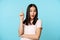 Creative korean girl raising finger up, eureka gesture, showing advertisement, looking surprised, standing over blue