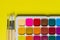 Creative layout with aquarelle palette, paint brushes on yellow background. Top view. Artists concept, copy space for text