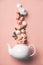 Creative layout made of whte tea pot with orange roses and merengues on pink background
