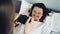 Creative man posing in bed with funny faces while woman taking photo with camera