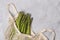 Creative minimal composition of fresh green asparagus in string bag on gray concrete background with copy space